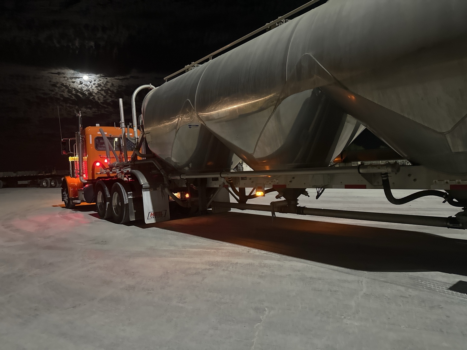 Anthony's orange Peterbilt and pneumatic bulk trailer under a cloud-streaked moon